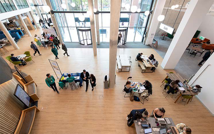 Top down view of the student centre foyer, with lots of people working on desks and walking around the open space.